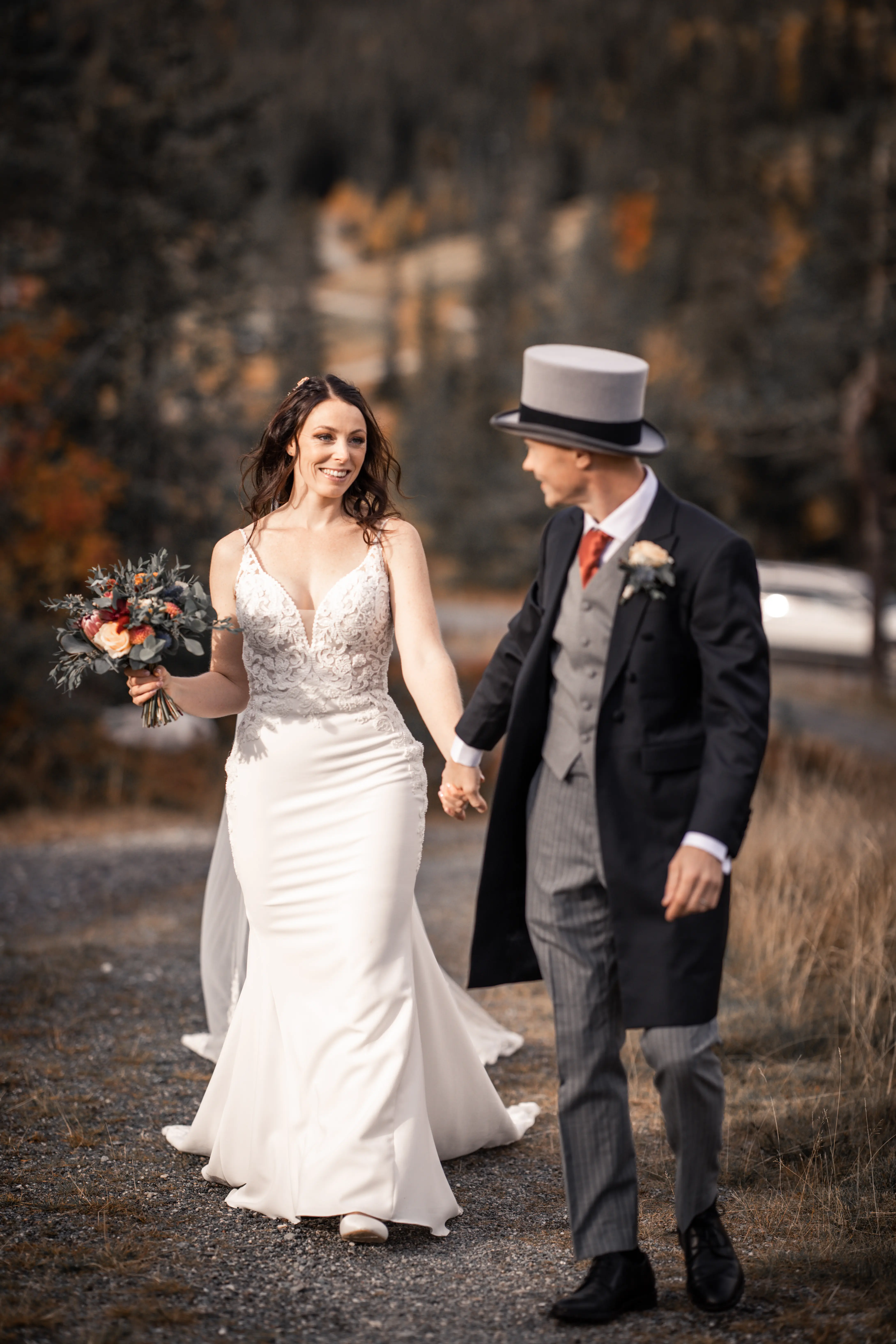 Bride wearing wedding dress called Nikki holding hands with her groom in a top hat.